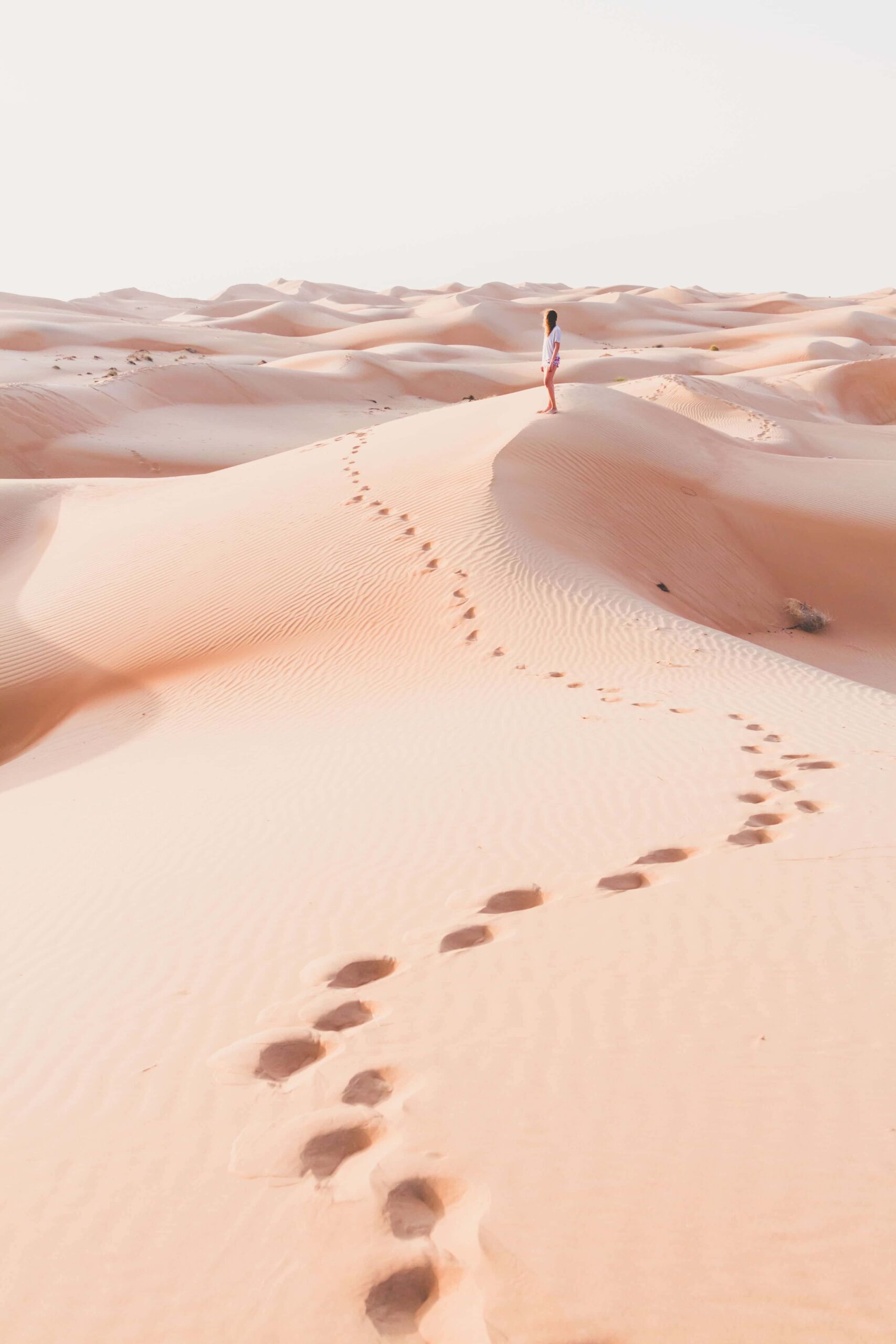 Blonde female Caucasian traveler leaving footprints in sand dunes when walking in dessert in Oman 67 1 min 1 scaled